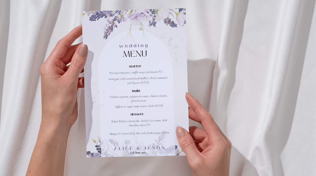Hands holding a wedding menu card with floral design against a white curtain background